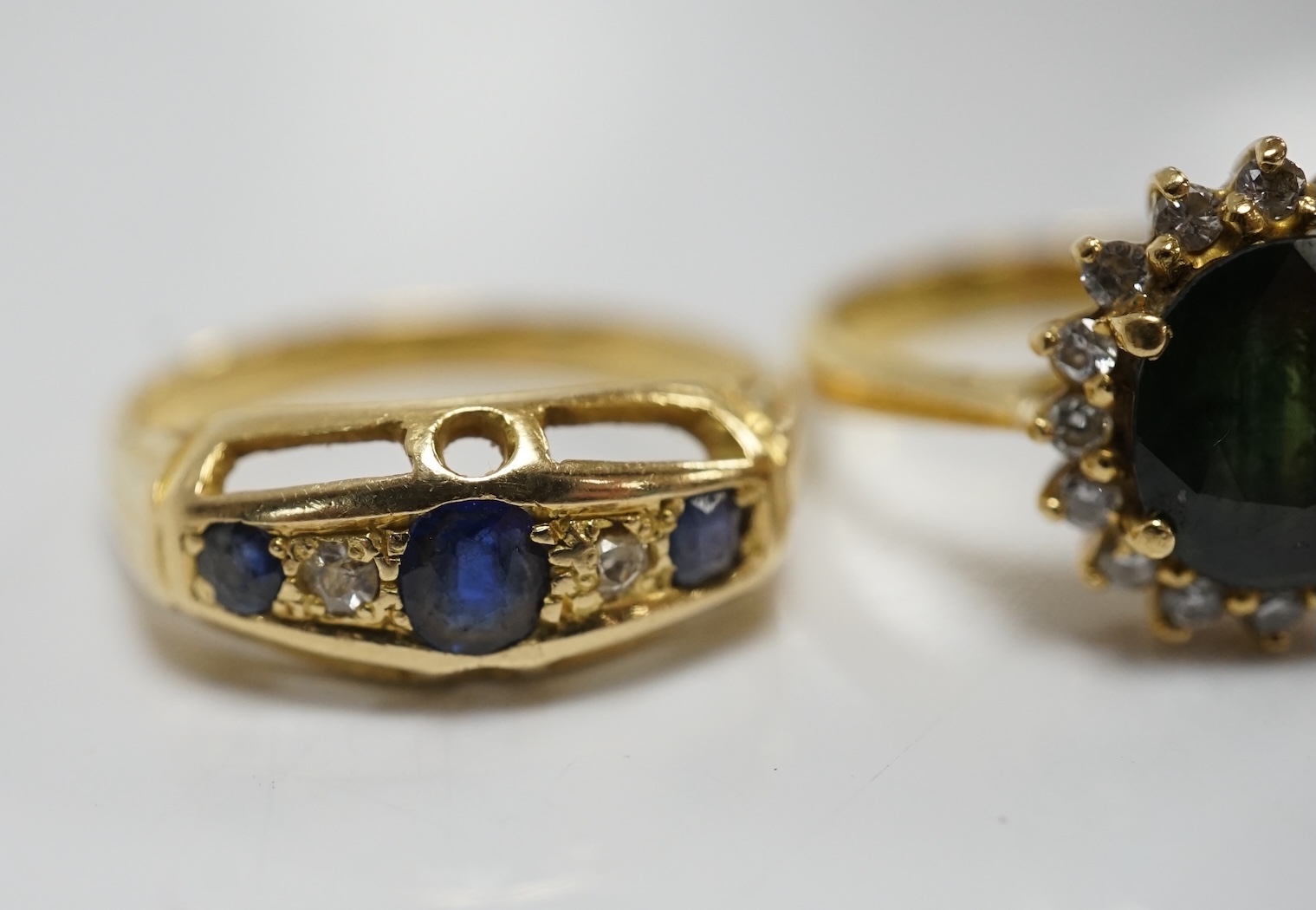 Two yellow metal and gem set rings, including a sapphire? and diamond oval cluster and a three stone sapphire and two stone diamond half hoop, gross weight 7.3 grams. Condition - poor to fair